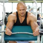 Grave bodybuilder in black jersey sits on exercise machine and r