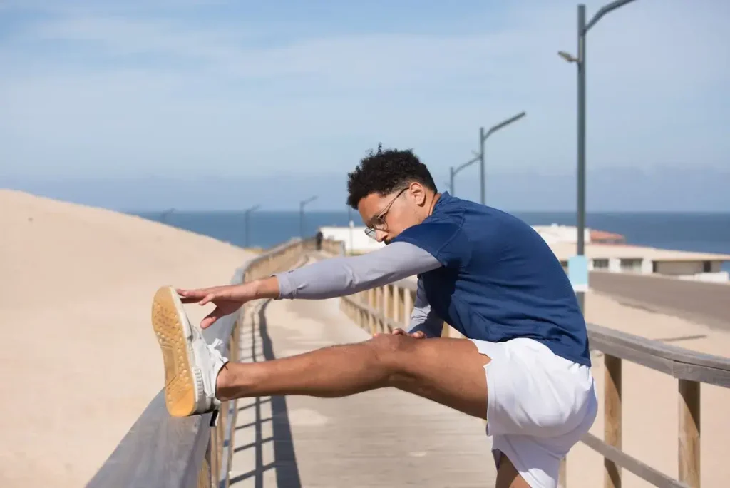 Young fitness enthusiast man stretching on the pier by the beach