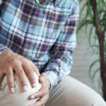 A middle aged man holding onto his painful knee while sitting.